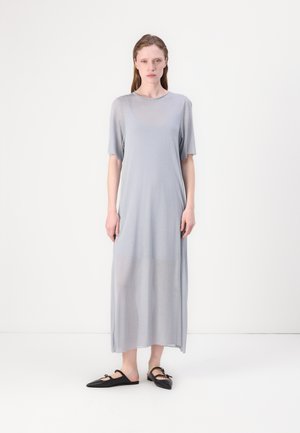 Graues, langes, locker sitzendes Kleid mit kurzen Ärmeln und rundem Halsausschnitt; leichtes Material mit leichtem Glanz; kombiniert mit schwarzen flachen Schuhen.