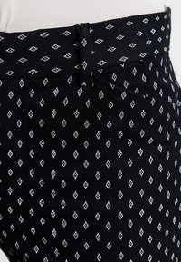 Pantalons noirs à motifs avec un design de diamants blancs. Fabriqués en tissu texturé, avec une taille ajustée et des détails de couture subtils.