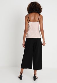 Camisola rosa con spalline nere regolabili, aderente nella parte superiore, che si apre in uno stile morbido; abbinata a pantaloni neri larghi e scarpe con tacco.