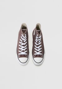 Zapatillas deportivas altas marrones con cordones blancos, puntera redonda, suela de goma negra y costuras blancas en contraste. Presenta ojales de metal y un parche con el logotipo.