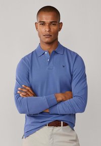 Polo tričko s dlhým rukávom v jednofarebnej svetlomodrej bavlne s golierom, tromi gombíkmi a malým čiernym logom na ľavej strane hrudníka.