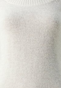 Gaišbeige adīta džempera ar ribotu apkakli, mīkstu tekstūru un bezšuvju dizainu ar nelielām krāsu variācijām visā virsmā.