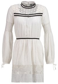 Biała sukienka z wysokim koronkowym dekoltem, długimi bufkami i czarnym paskiem w talii. Posiada skomplikowane wzory koronkowe w całej długości.