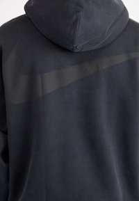Felpa con cappuccio nera dal tessuto morbido, con un grande logo Nike swoosh tonale sul retro. Design semplice e moderno.