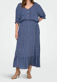 Abito lungo blu navy con pois bianchi. Presenta un collo a V, maniche a sbuffo corte e un orlo a balze a strati. Tessuto morbido con una vestibilità comoda.