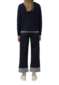 Marineblauw gebreid sweater met ronde hals, gecombineerd met donkere denim wijde broek met lichtblauwe manchetten. Draag met witte platform sneakers.