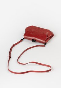 Red leather crossbody bag with a smooth texture, a folded design, and a detachable strap. Features black hardware accents.