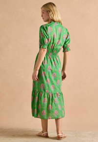 Zielona midi sukienka w kwiaty z bufkami, elastyczną talią i falbaną na dole. Cechuje się różowymi i fioletowymi wzorami kwiatowymi na teksturowanej tkaninie.