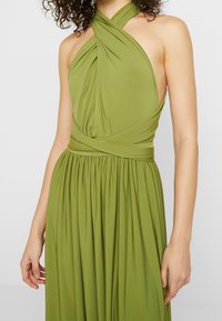 Robe verte à col licou avec un corsage drapé, un design croisé au niveau de l'encolure et une jupe plissée pour une apparence fluide.