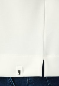 Weißes Kurzarmhemd mit geradem Saum. Verfügt über ein kleines schwarzes Logo-Tags auf der unteren linken Seite und dezente Nähte.