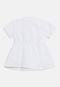 Λευκό μπλουζάκι με κοντά μανίκια, ζώνη στη μέση με σούρες και διακριτικές κάθετες ρίγες, απλωμένο επίπεδα σε λευκό φόντο.