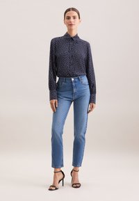Blusa blu navy con pois bianchi, design con bottoni, abbinata a jeans azzurri a vita alta e tacchi a spillo neri.