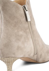 Stivale alla caviglia in suede beige con zip laterale, tacco texturizzato e punta affusolata. Il tacco presenta un design intrecciato per un tocco di dettaglio in più.
