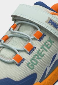 Κοντινό πλάνο αθλητικού παπουτσιού με λευκή λωρίδα, ελαστικά γκρι κορδόνια με πορτοκαλί λεπτομέρειες, ετικέτα GORE-TEX και μπλε και πορτοκαλί λεπτομέρειες στη σόλα.