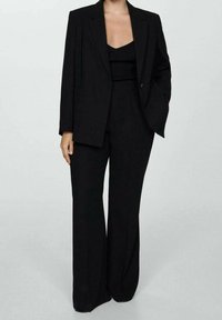 Blazer noir ajusté avec des revers marqués, porté sur un haut noir ajusté. Associé à un pantalon large noir, mettant en valeur une silhouette épurée.