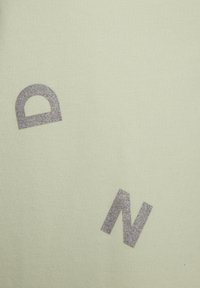 Tessuto verde chiaro con una texture morbida presenta lettere argentate glitterate "D" e "N" stampate in uno stile moderno e blocco.