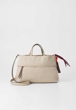 Beige canvas handbag with brown leather accents, two top handles, detachable shoulder strap, and decorative braided tassel.
