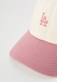 Cap with a cream fabric body and a pink textured brim. Features embroidered "LA" logo in pink on the front.