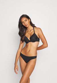 Ensemble de lingerie noire comprenant un soutien-gorge plongeant avec des fines bretelles réglables et un bikini taille basse assorti. Tissu doux avec un léger éclat.