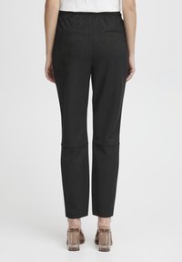 Zwarte, stretchy broeken met een slim fit, voorzien van zijnaad en elastische tailleband. De stof heeft een gladde textuur en twee achterzakken.