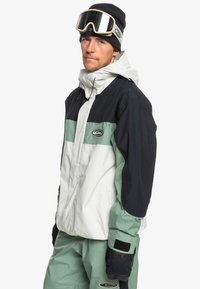 Schneejacke mit einem Drei-Farben-Design: Schwarz, Weiß und Minzgr�ün. Hergestellt aus wasserabweisendem Material mit hohem Kragen und verstellbaren Bündchen.
