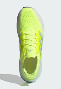 Neona dzeltena sporta apavu ar režģa augšdaļu, teksturētu dizainu, polsterētu apkakli un trim atstarojošām svītrām. Ar "ULTRABOOST" raksturu zolē.