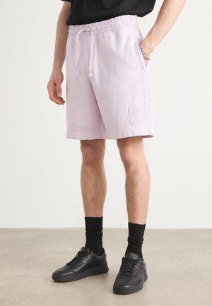 Light lavender cotton shorts with an elastic waistband and drawstring, featuring embroidered "HUGO" logo on the leg. Styled with black sneakers.