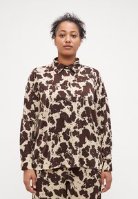 Halenka s dlouhým rukávem v béžovém a hnědém cow printu, s límečkem a knoflíkovým zapínáním, vyrobená z hladkého a jemného materiálu.
