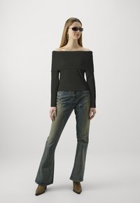 Top a coste nera senza spalle, abbinato a jeans svasati blu chiaro. La modella indossa occhiali da sole con montatura quadrata e stivali col tacco color sabbia.