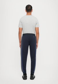 Pelēks īsu piedurkņu krekls un tumši zili treniņbikses ar zils un pelēks sānu svītrām, elastīgs jostasvieds, apakšā salocīti gali un melnas kurpes.