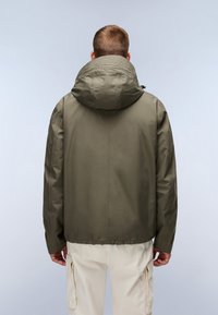 Olive green wodoodporna kurtka z wysokim kołnierzem i kapturem na sznurku. Posiada gładką fakturę i luźny krój, w połączeniu z kremowymi spodniami cargo.