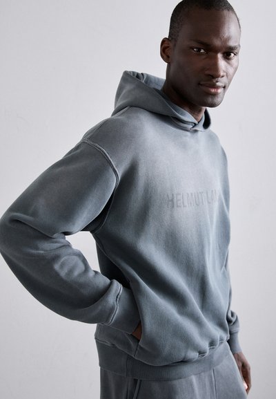 Hallin musta pehmeast puuvillasegust kangast, millel on känguru tasku, ribatud varrukad ja üksildane tekst "HELMUT LANG" kergelt sisse pressitud esiküljel.