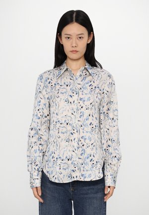 Bloemenblouse met lange mouwen, versierd met blauwe en zwarte bladpatronen op een lichtbeige achtergrond, met een klassieke kraag en knoopsluiting aan de voorkant.