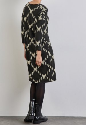 Vestido de punto negro con patrón abstracto crema, mangas tres cuartos y corte holgado, combinado con botas negras hasta el muslo.