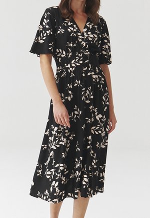 Zwarte jurk met korte uitlopende mouwen, knopen aan de voorkant en een lichte bloemenprint. Vloeiende stof en een lengte tot op de knie met een accentueerde taille.