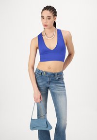 Blå ribbete crop-top med dyp V-hals, kombinert med lyseblå utsvingte jeans; holder en liten blå denimhåndveske.