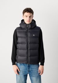 Zwarte puffer vest met een rits aan de voorkant en een afneembare capuchon. Bevat gestikte panelen, subtiel logo en een gladde, glanzende textuur.