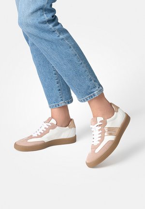 Person wearing light blue jeans and beige-white sneakers with white laces, mid-step on a plain white background.