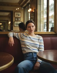 Suéter a rayas en crema, azul y marrón; textura acanalada. Jeans de denim de tiro alto. El escenario presenta una pared espejada y un acogedor reservado.