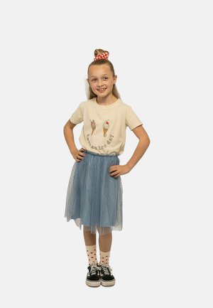T-shirt beige chiaro con stampa di coni gelato, abbinato a una gonna in tulle blu. Sneakers nere e calzini bianchi a fantasia con cuori rossi.