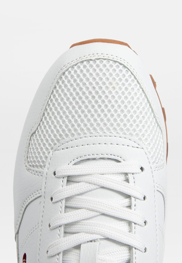 Sneaker bianca con materiale in rete testurizzata sulla punta, lacci piatti e suola in gomma con un accento marrone a contrasto.
