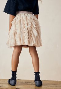 Jasnoróżowa, warstwowa spódnica z tiulu o falbaniastej strukturze, z akcentowanym pasem. Połączona z czarnymi, błyszczącymi butami i teksturowanymi skarpetkami.