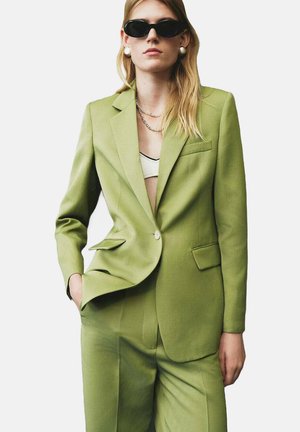 Green blazer and matching pants made of textured fabric. Blazer features a single button, notched lapels, and a breast pocket.