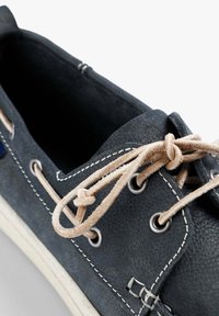 Granatowe skórzane buty żeglarskie z beżowymi sznurówkami, metalowymi oczkami i białą gumową podeszwą. Posiadają fakturowaną powierzchnię i kontrastowe przeszycia.