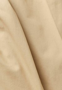 Béžová bavlněná látka s hladkým textura, vykazující jemné záhyby a stíny, což naznačuje měkký, lehký materiál.