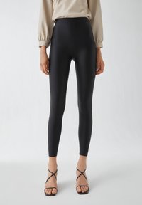 Zwarte high-waisted leggings van een gladde, rekbare stof, met een strak ontwerp en een getailleerde pasvorm.