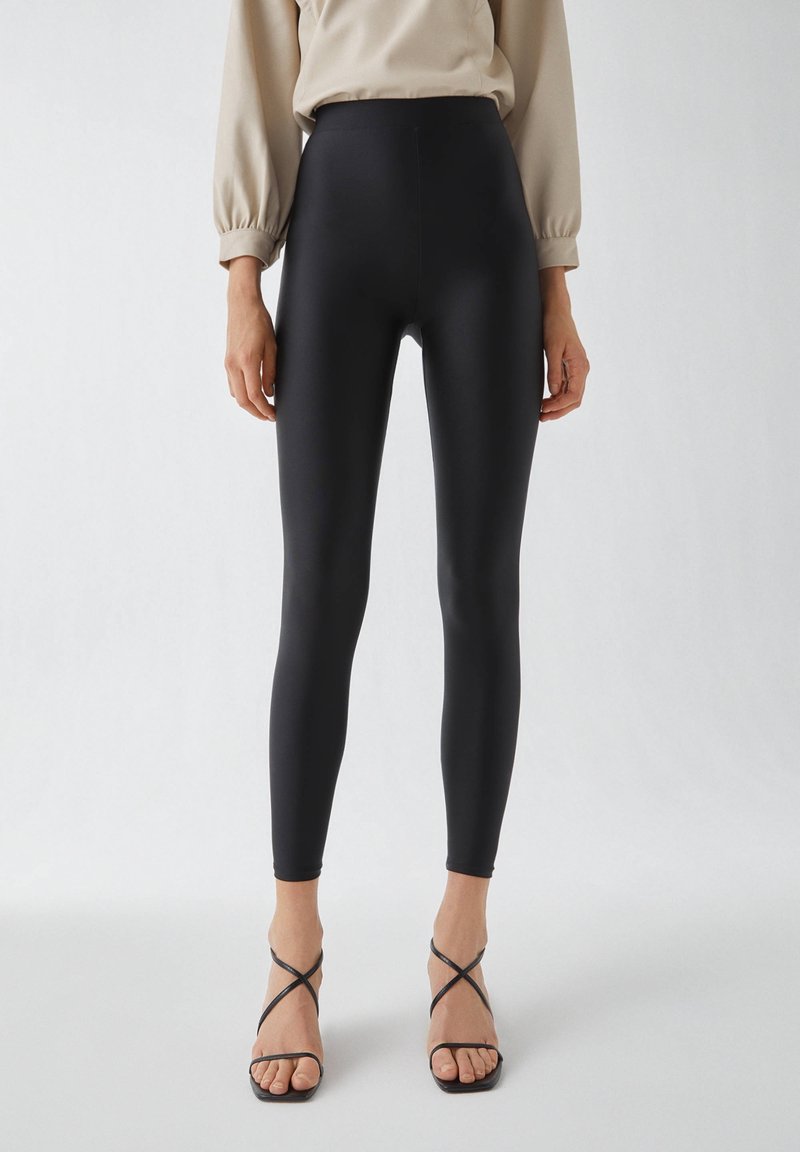 Zwarte high-waisted leggings van een gladde, rekbare stof, met een strak ontwerp en een getailleerde pasvorm.