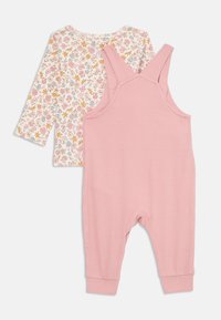 Pink ribbed overalls with adjustable straps paired with a long-sleeve shirt featuring a floral pattern in pink, yellow, and blue tones.