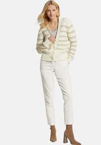 Lichte crèmekleurige cardigan met horizontale strepen, gestructureerd breiwerk, ribbelzoom en manchet, gecombineerd met witte cropped broeken en bruine enkellaarsjes met hak.