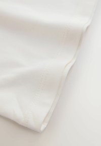 Bílá bavlněná látka s hladkou texturou, s čistými švy podél okrajů a mírným strečem.